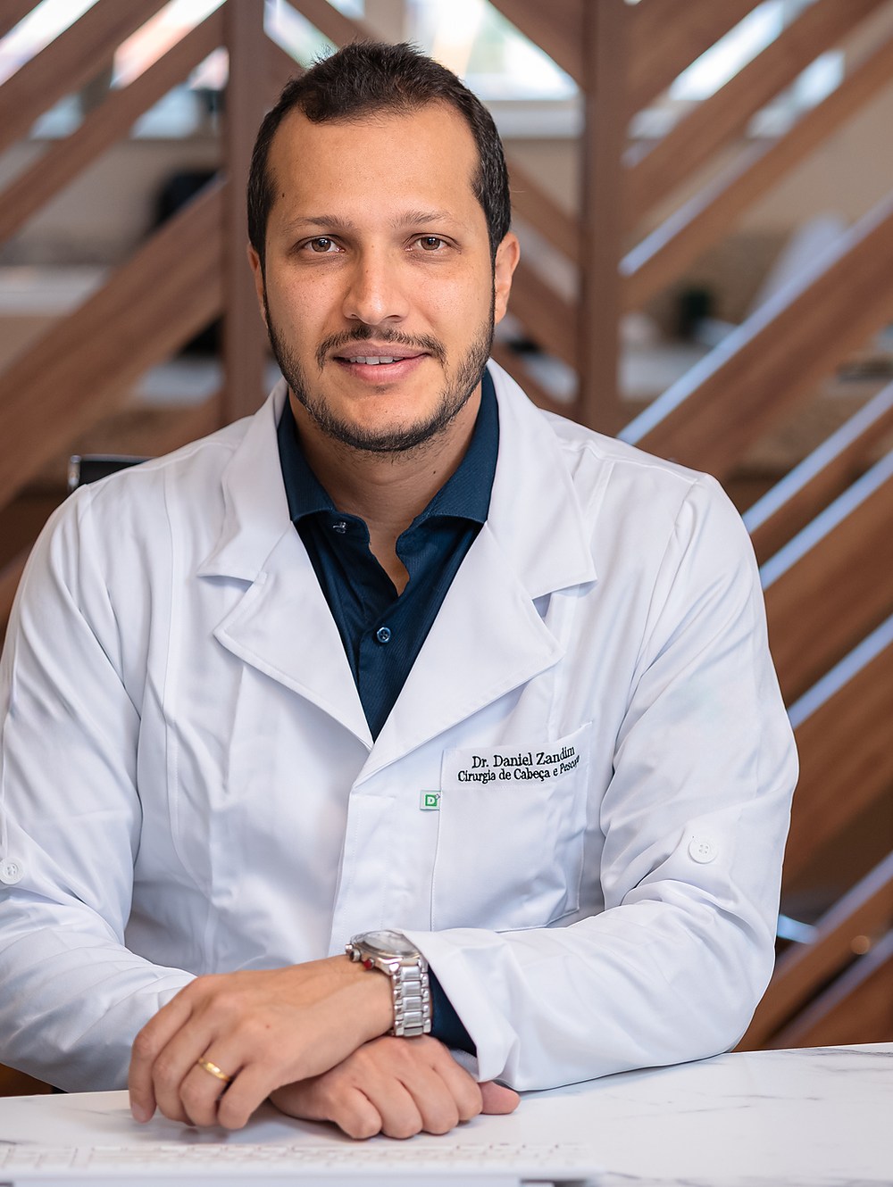 Dr. Daniel Zandim sentado em seu consultório, vestindo jaleco branco